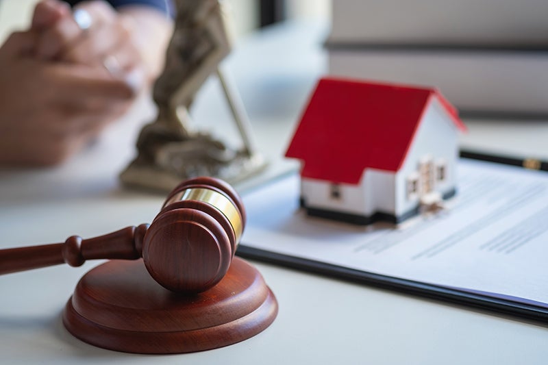 A gavel, miniature house, and legal document on a desk, representing property law or real estate disputes.