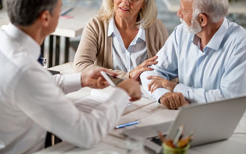 Financial advisor showing something on a tablet to two senior clients (man and woman) at a table.