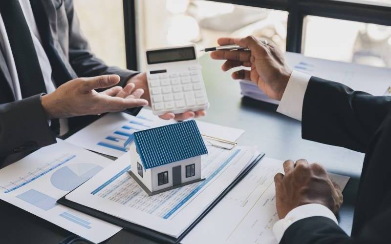 Two people discussing home finances and mortgage rates, with a calculator, documents, and small model house on the table.