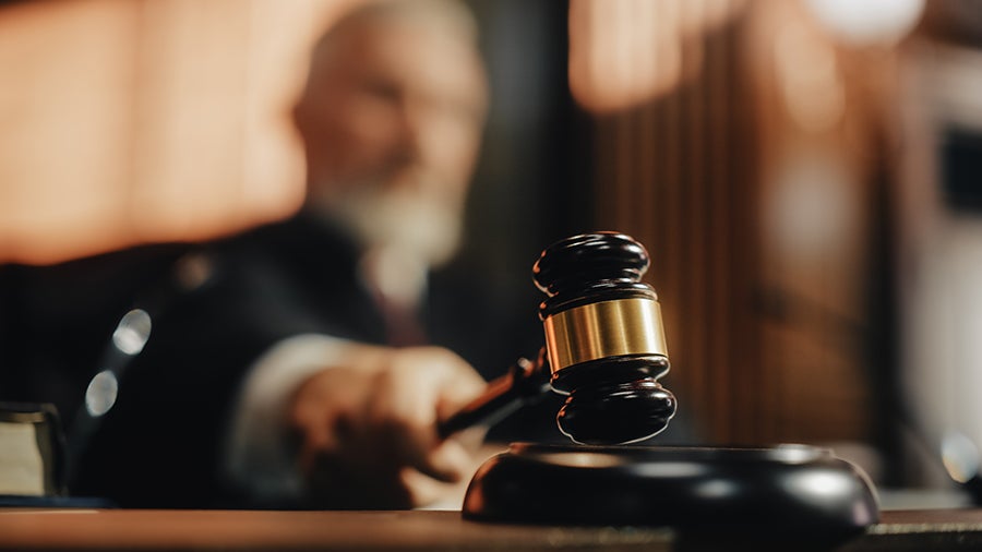 A judge or auctioneer pounds a wooden gavel with a golden band on a dark block.