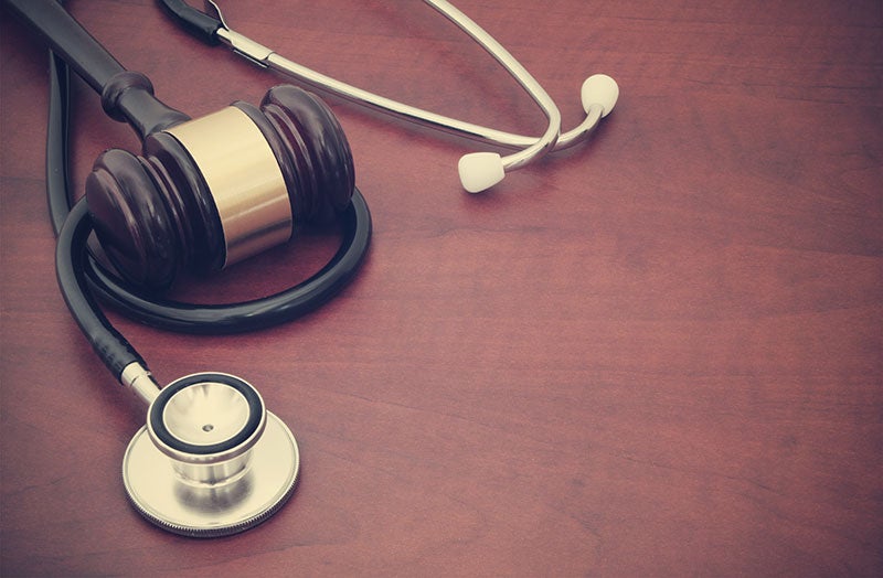 A judge's gavel and a stethoscope resting on a deep red wooden surface, symbolizing legal and medical fields.