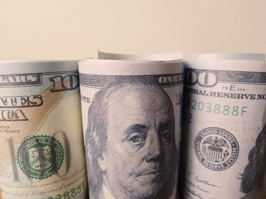 Three rolls of US hundred dollar bills, with Benjamin Franklin's portrait visible on the central roll.