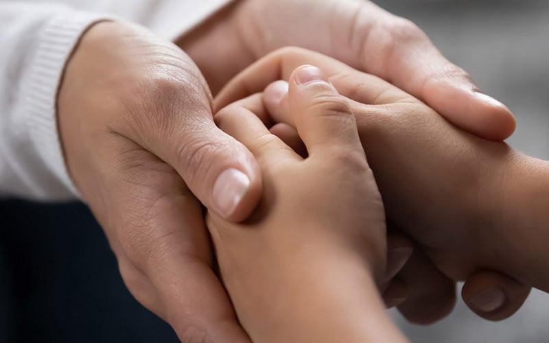 An adult's hands gently holding a child's hands, illustrating care and connection.